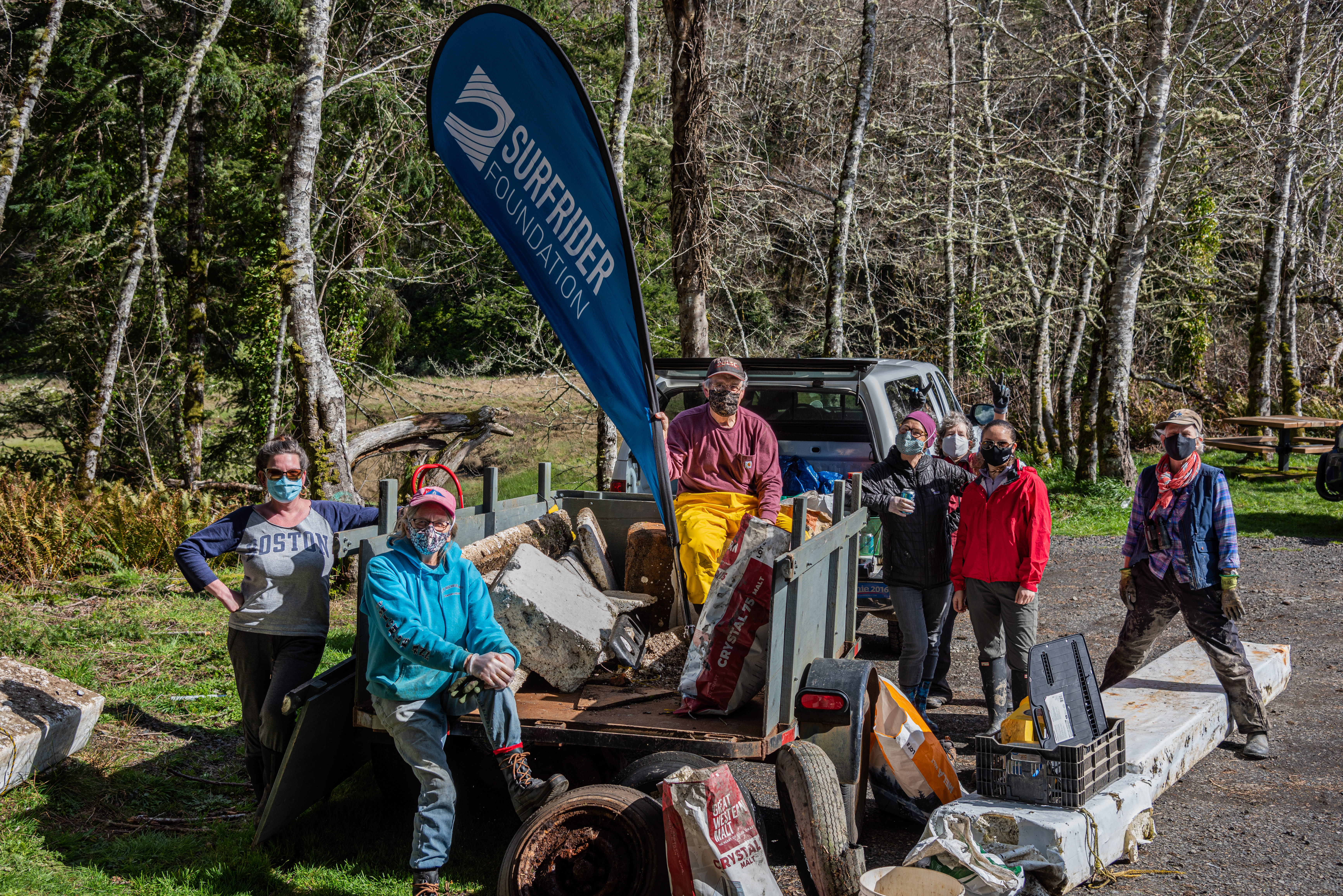 Six volunteers gather near a wooden area with a truck with with supplies for a restoration project